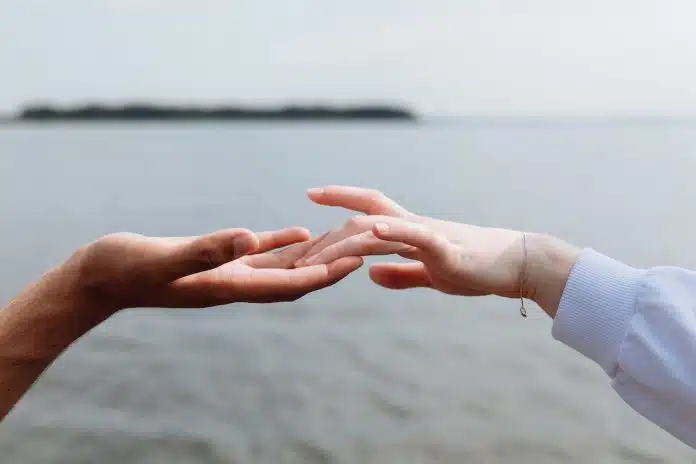 Dos manos tocándose de los dedos frente al mar