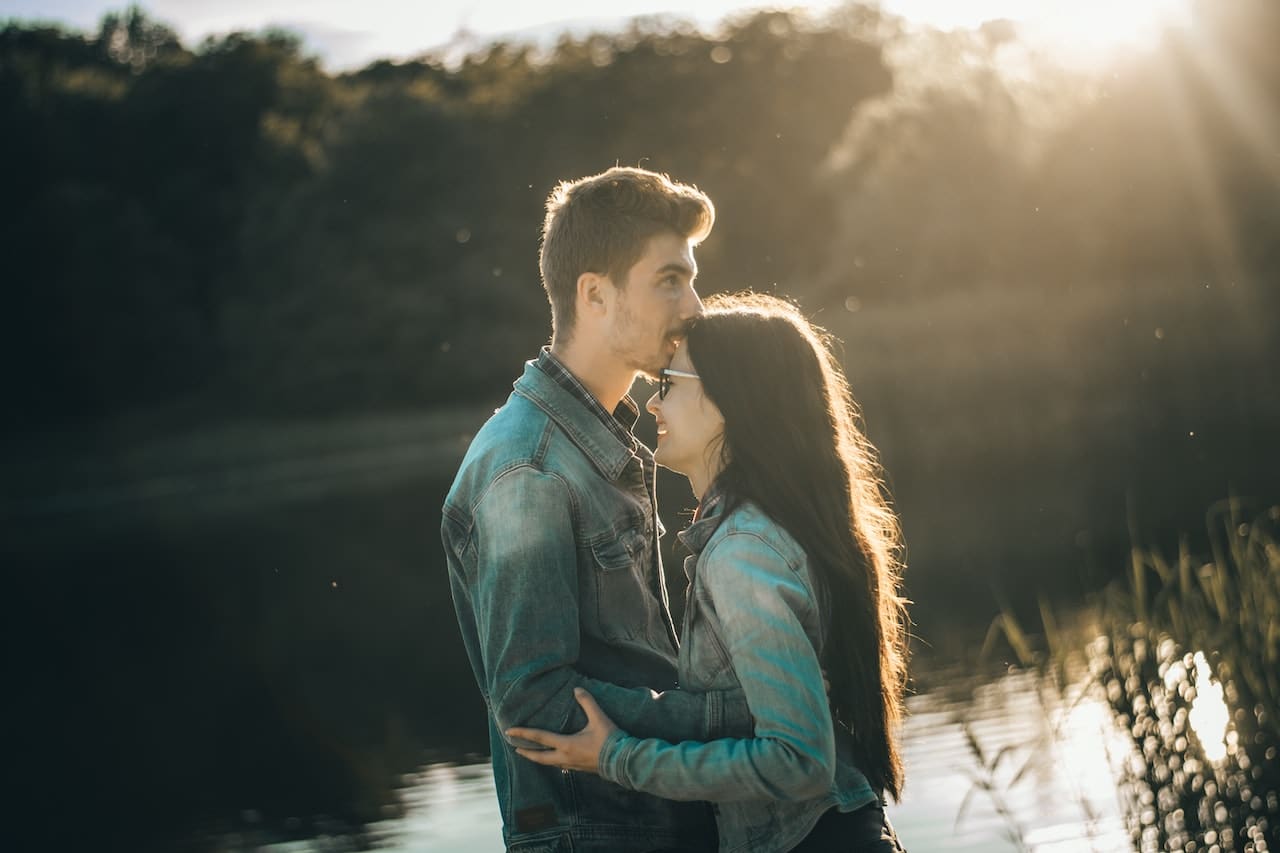 Hombre besando en la frente a su pareja en un lago
