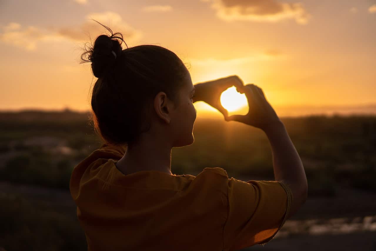 Mujer formando corazón con manos en puesta de sol
